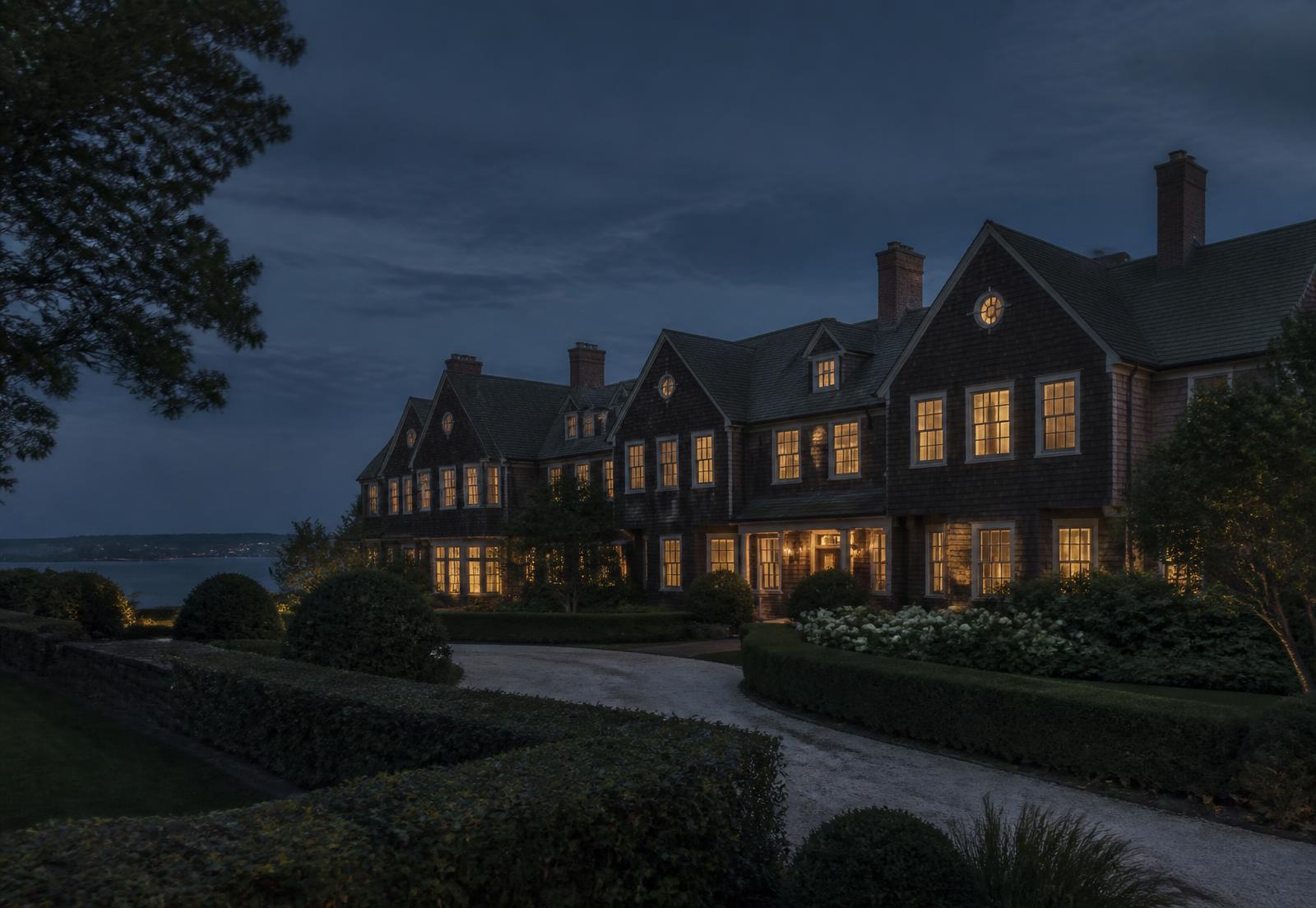 A New England shingle-style estate at twilight with warmly lit windows